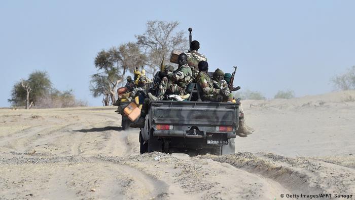 Nigerian soldiers traveling on the back of a pick-up truck.