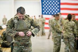 A American soldier puts on military gear in front of a US flag
