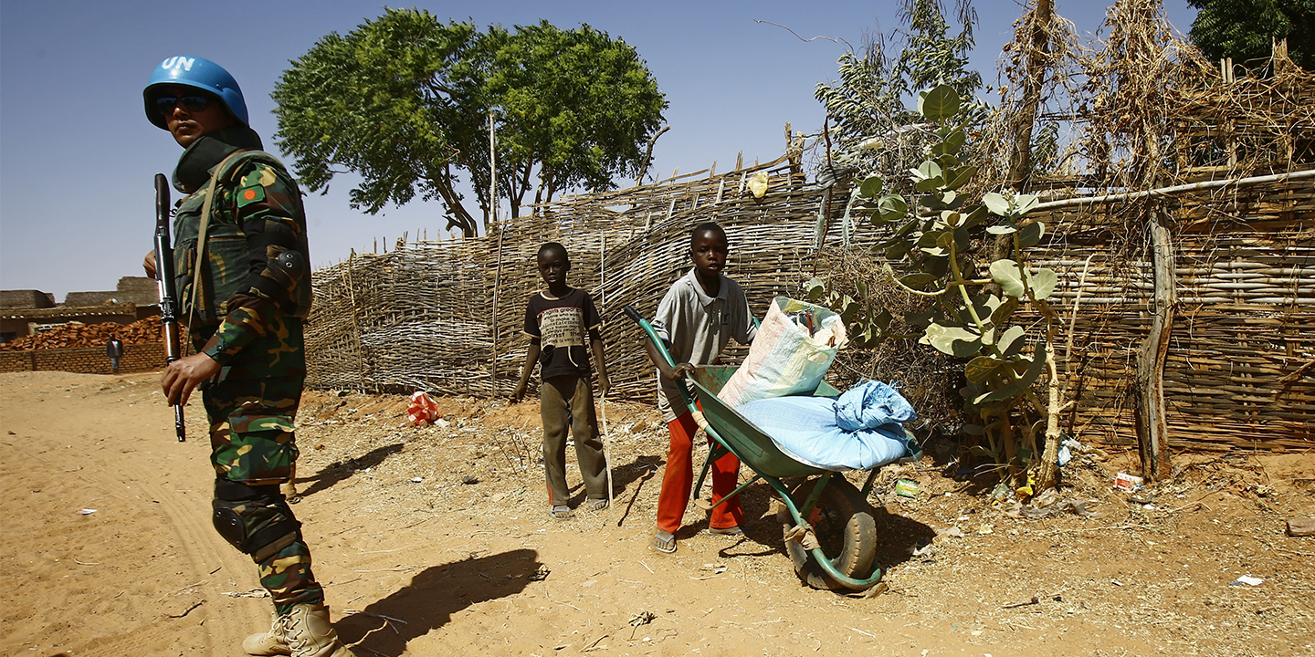 Sudanese boys push a wheelbarrow past a United Nations peace keeper at the El-Riyadh camp for internally displaced persons in el-Geneina, on February 8, 2017
