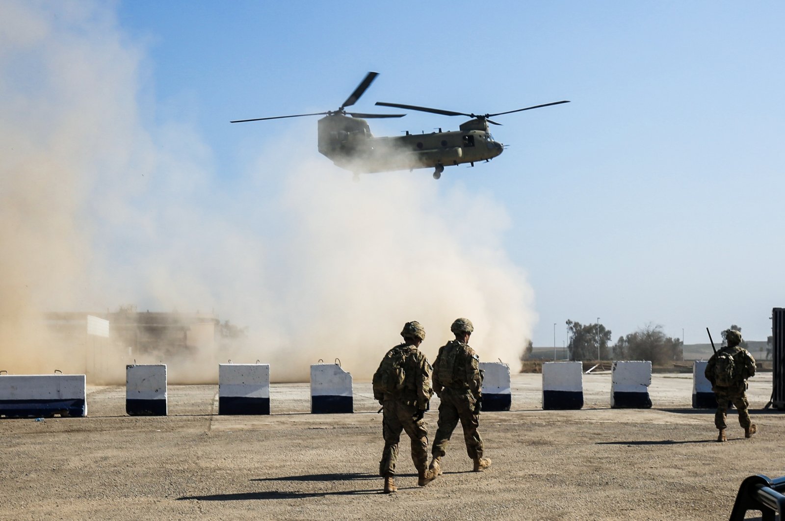 American troops walk as a US Army C-47 Chinook helicopter flies over the village of Oreij, south of Mosul, Iraq