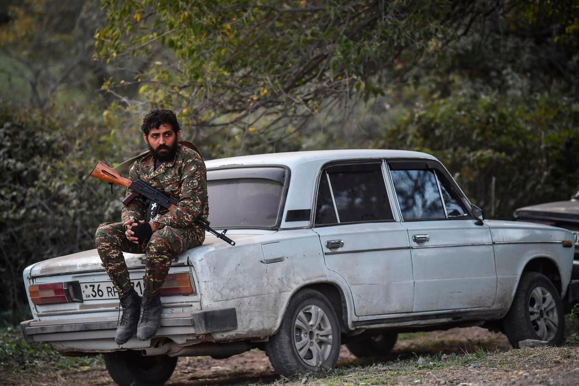 A volunteer fighter sits on a car as cannons fire nearby