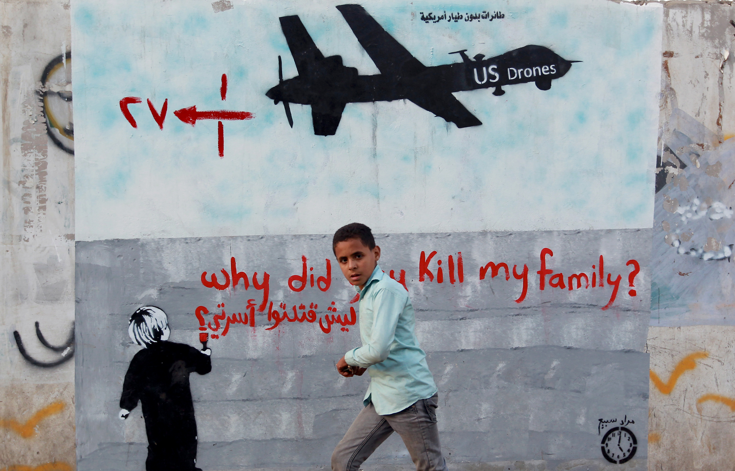 A Yemeni boy walks past a mural depicting a US drone and reading 