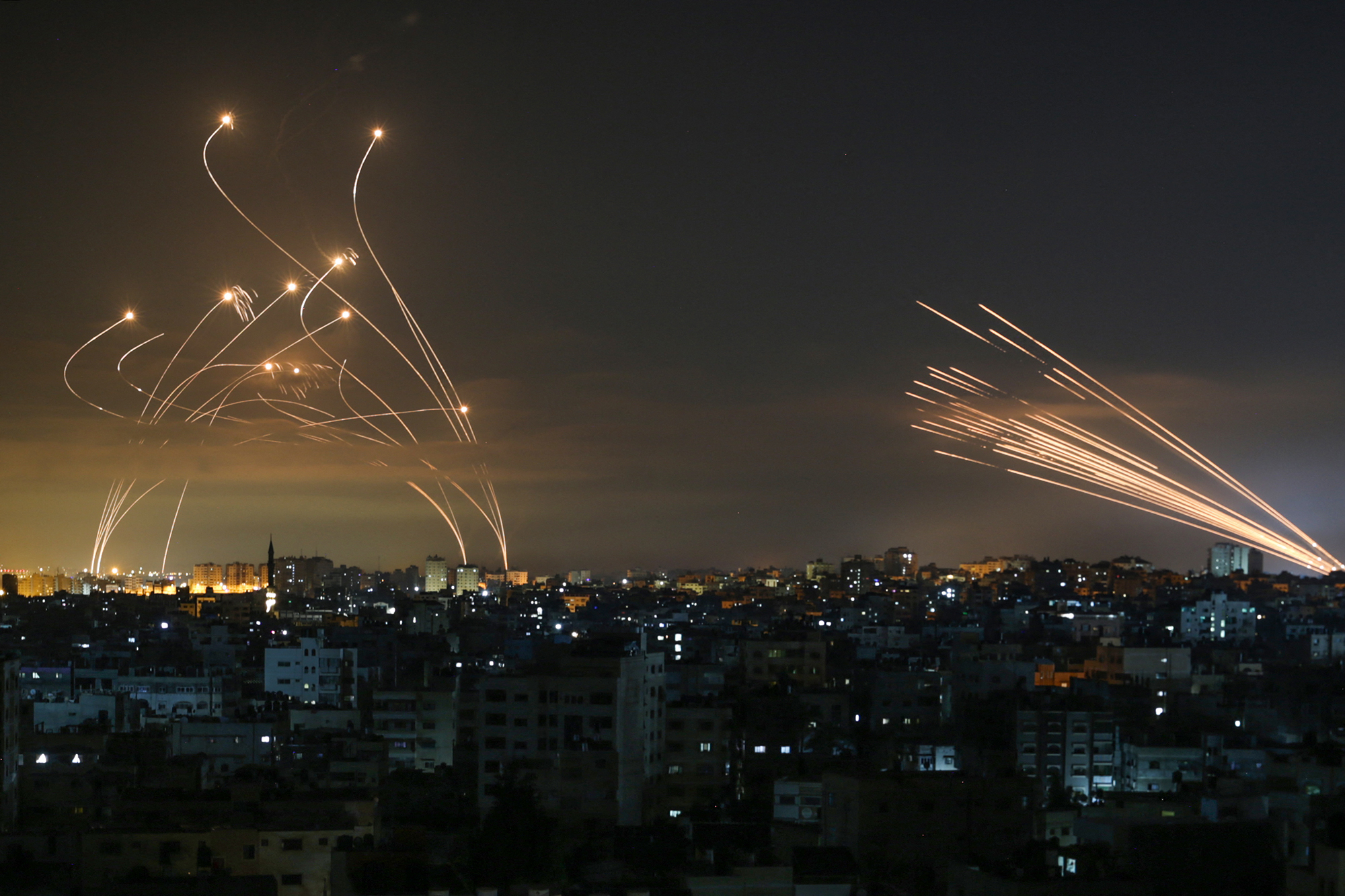 The Israeli Iron Dome missile defense system, left, intercepts rockets fired from Gaza Strip