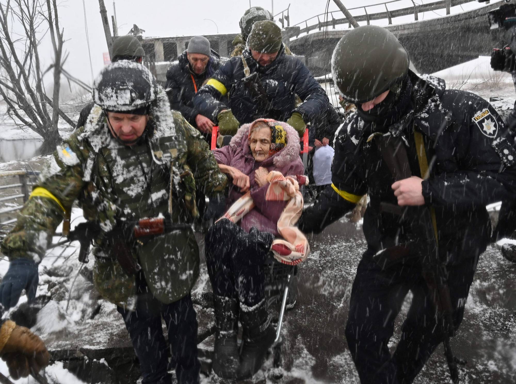 Ukrainian soldiers help an elderly woman to cross a destroyed bridge