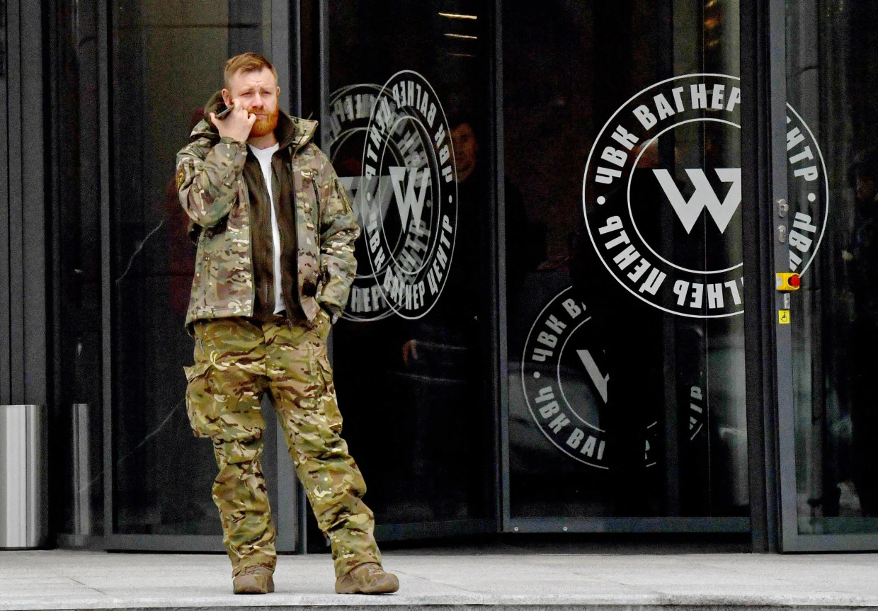 A man wearing military camouflage stands at the entrance of the PMC Wagner Centre, associated with the Wagner Group, in St. Petersburg, Russia