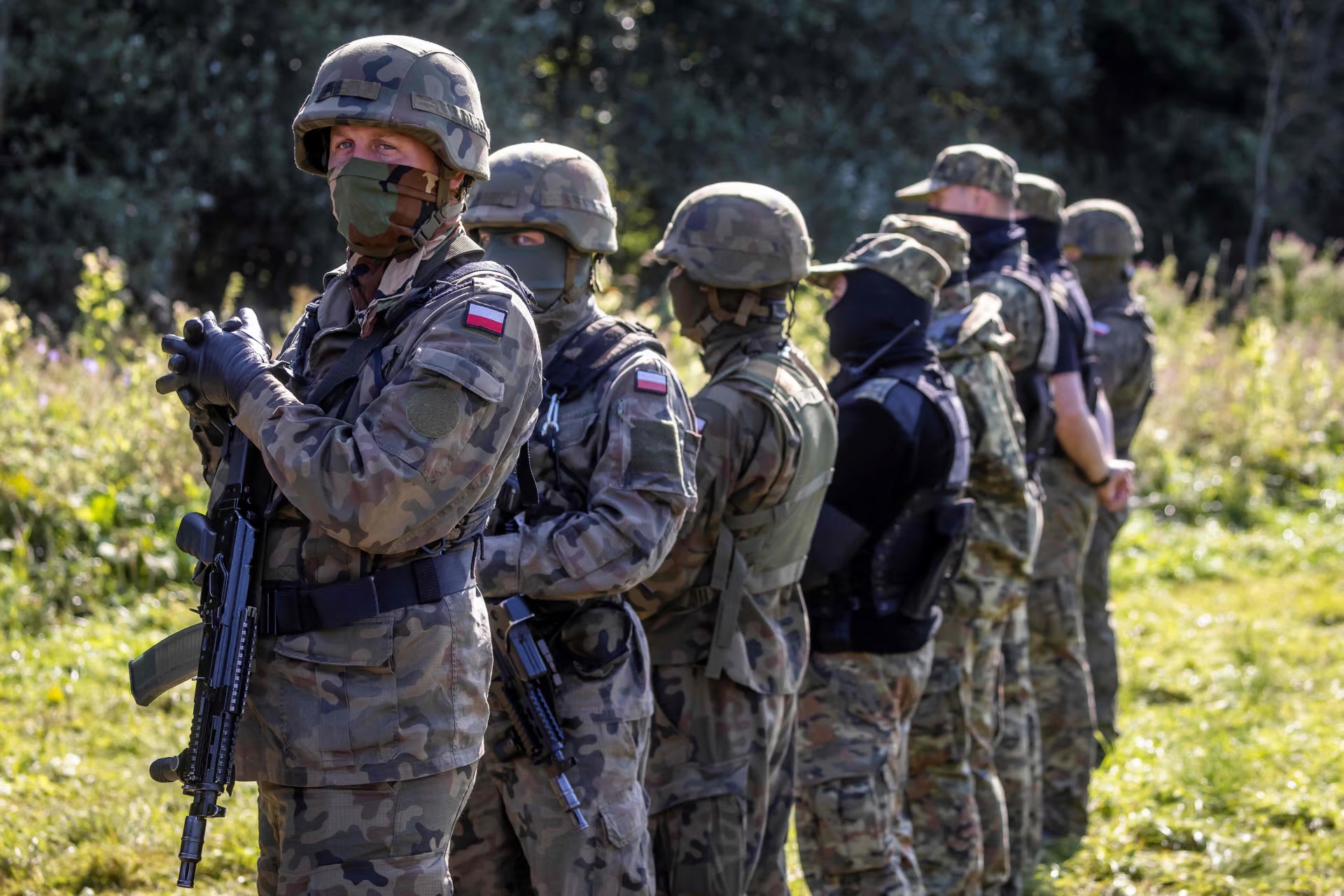 Armed Polish border guards stand next to a group of migrants on the border with Belarus