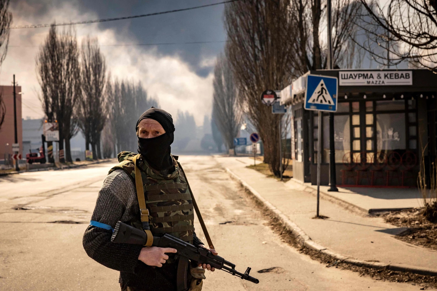 A Ukrainian serviceman stands guard near a burning warehouse hit by a Russian shell in the suburbs of Kyiv