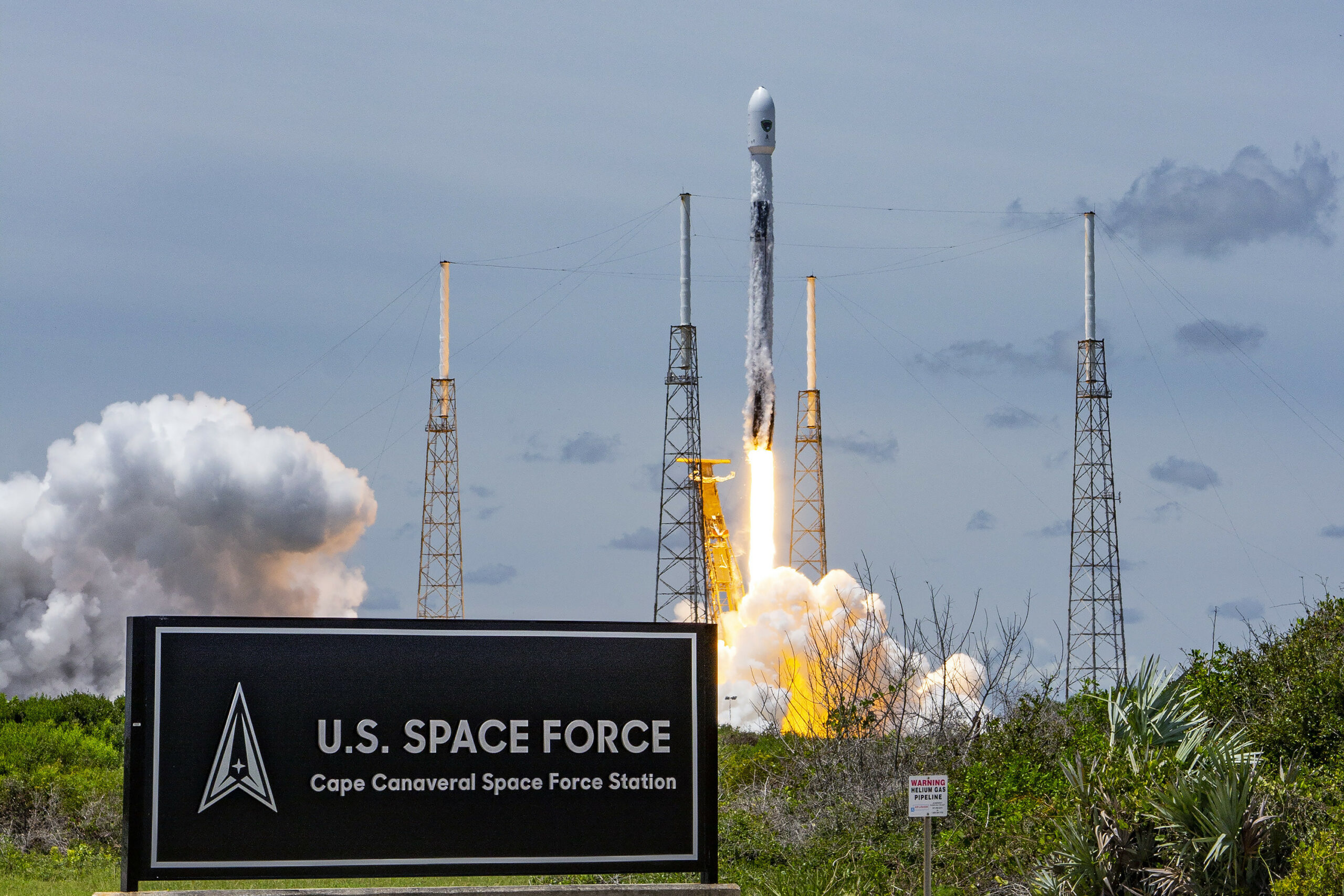 A rocket launches from at Cape Canaveral Space Force Station, Florida. On the left of the foreground, a sign that says 