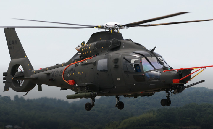 A dark green-colored light-armed helicopter is seen flying over a forest landscape.