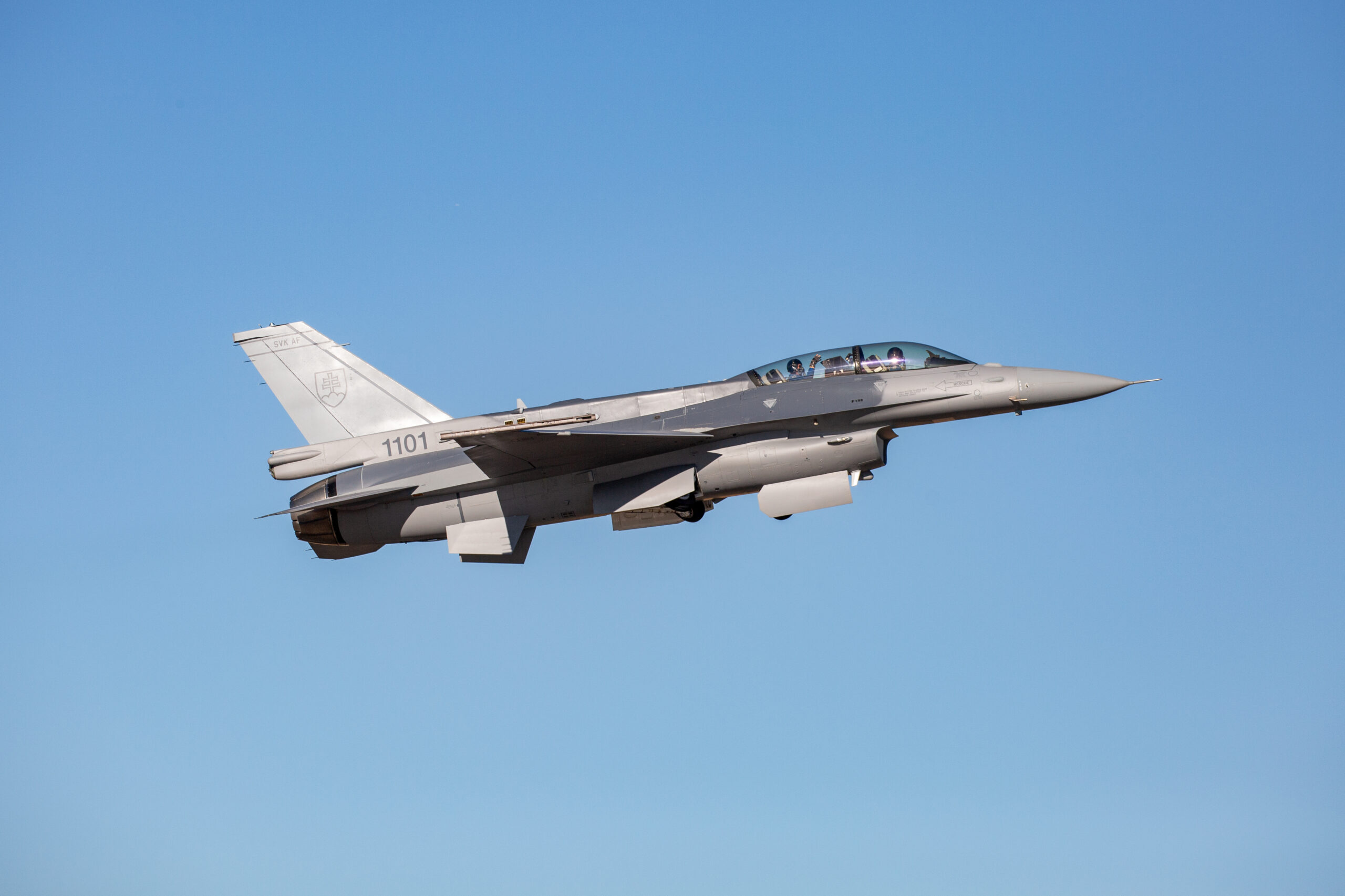 A gray Lockheed Martin F-16 jet plane is seen flying in clear blue skies. It has 