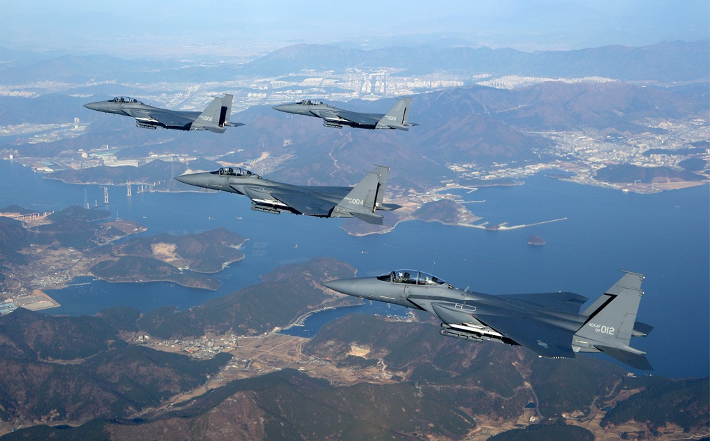 Four gray Republic of Korea Air Force fighter jets are seen flying high above a landscape with a wide, winding river passing through it.