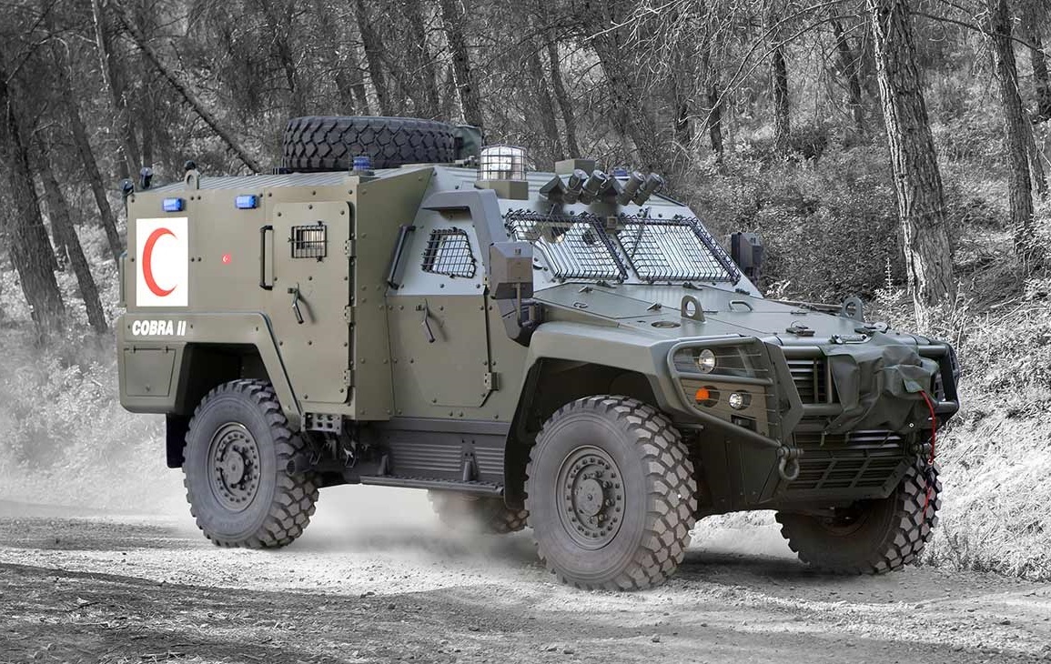 An Otokar Cobra II armored vehicle is seen driving around on a snowy forested area. Its green-gray paint blend in well with the environment.