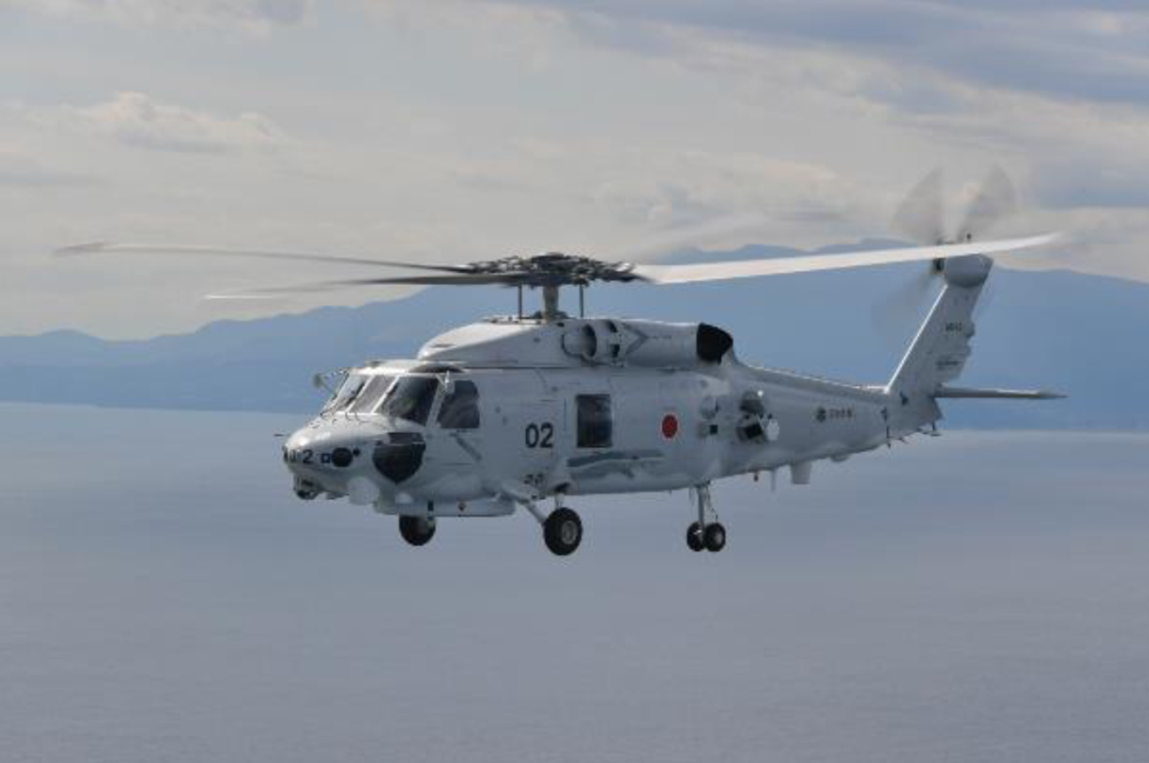 A Mitsubishi SH-60L is seen flying above the sea. The white-gray helicopter has 