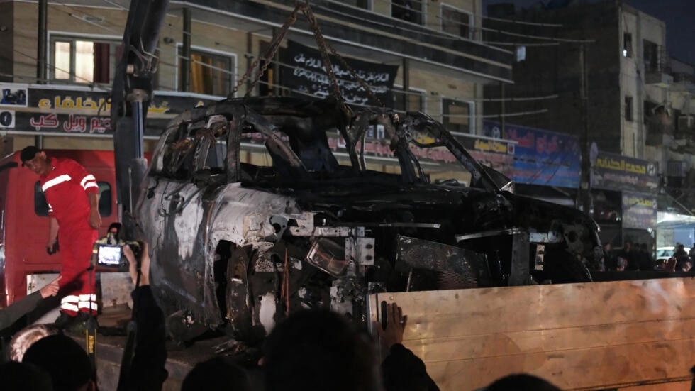 People watch as a vehicle that was hit by a deadly drone strike is removed from a Baghdad neighbourhood