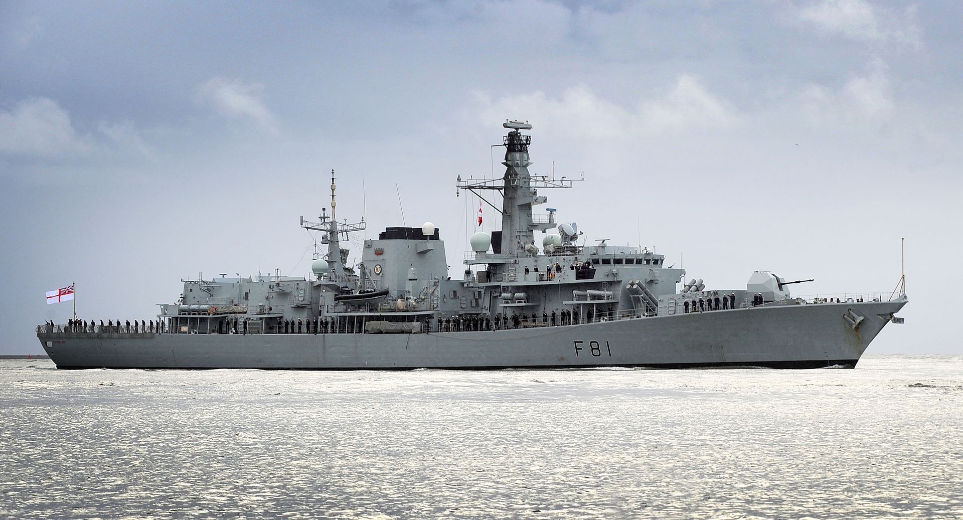HMS Sutherland, a UK Royal Navy frigate, is seen sailing on calm waters. The gray ship has 