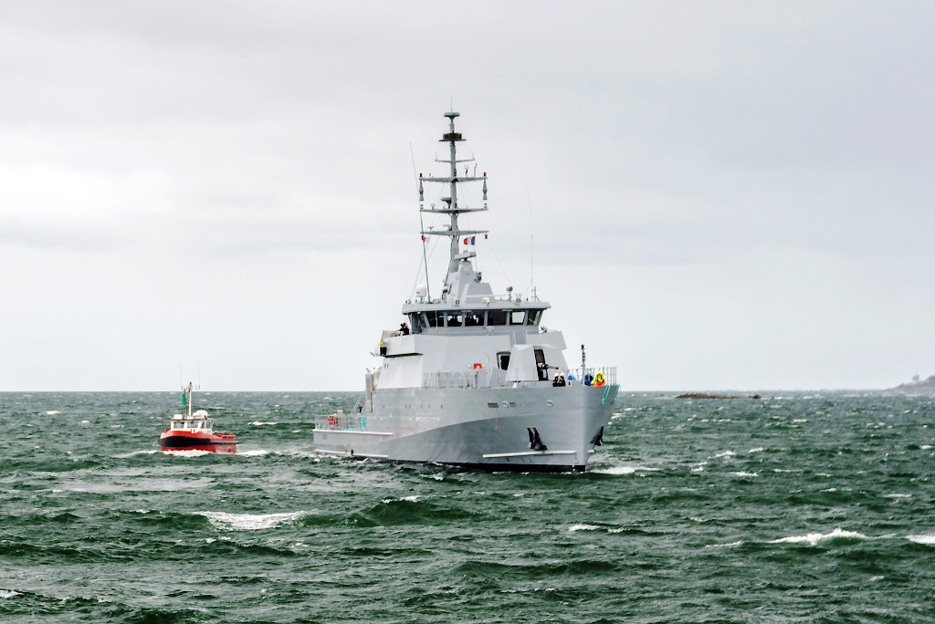 Cayor, a 58 S-class offshore patrol vehicle, is seen sailing in green-blue waters. The gray seacraft is accompanied by a much smaller red boat, which is sailing on its right side.