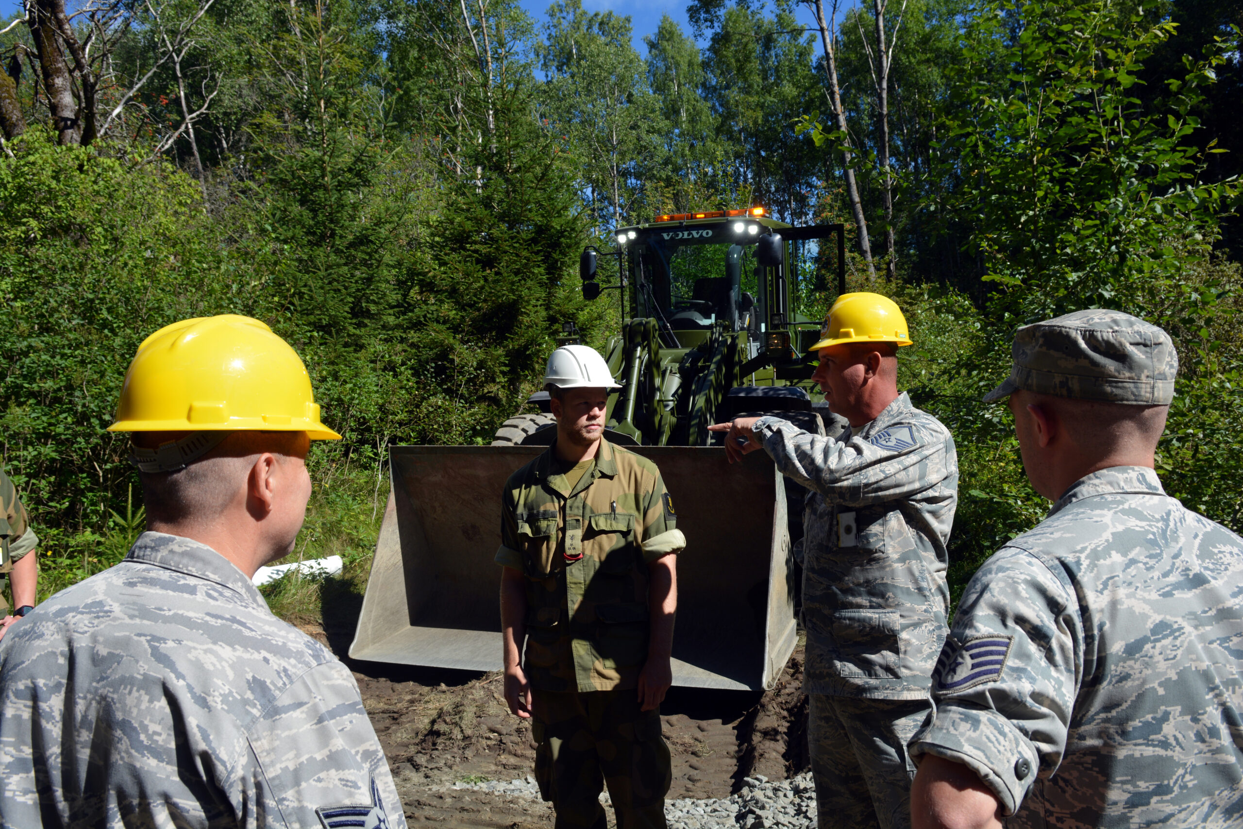 U.S. Air Force Master Sgt. Roy Combs (second from right), a heavy equipment operator with the Texas Air National Guard's 149th Civil Engineering Squadron, a subordinate unit of the 149th Fighter Wing, based at Joint Base San Antonio - Lackland, Texas, discusses the status of a construction project with Cadet Einar Drheim, a senior Royal Norwegian military cadet enrolled in the engineering program at the Norwegian Military Academy (Krigsskolen), at Camp Linderud, in Oslo, Norway, at Rygge Air Station, Norway, Aug. 14, 2013. The 149th Fighter Wing's 149th Civil Engineering Squadron was in Norway as part of the U.S. National Guard Bureau's deployment for training program to train with members of the Royal Norwegian armed forces. (U.S. Air National Guard photo by Staff Sgt. Phil Fountain / Released) (This image was modified to obscure personally identifiable information on the subject's identification badge for security and privacy reasons.)