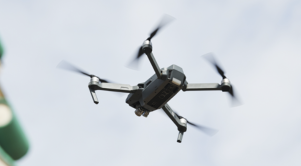 A black drone is seen hovering above. It has four propellers, each of them attached to the end of its four 