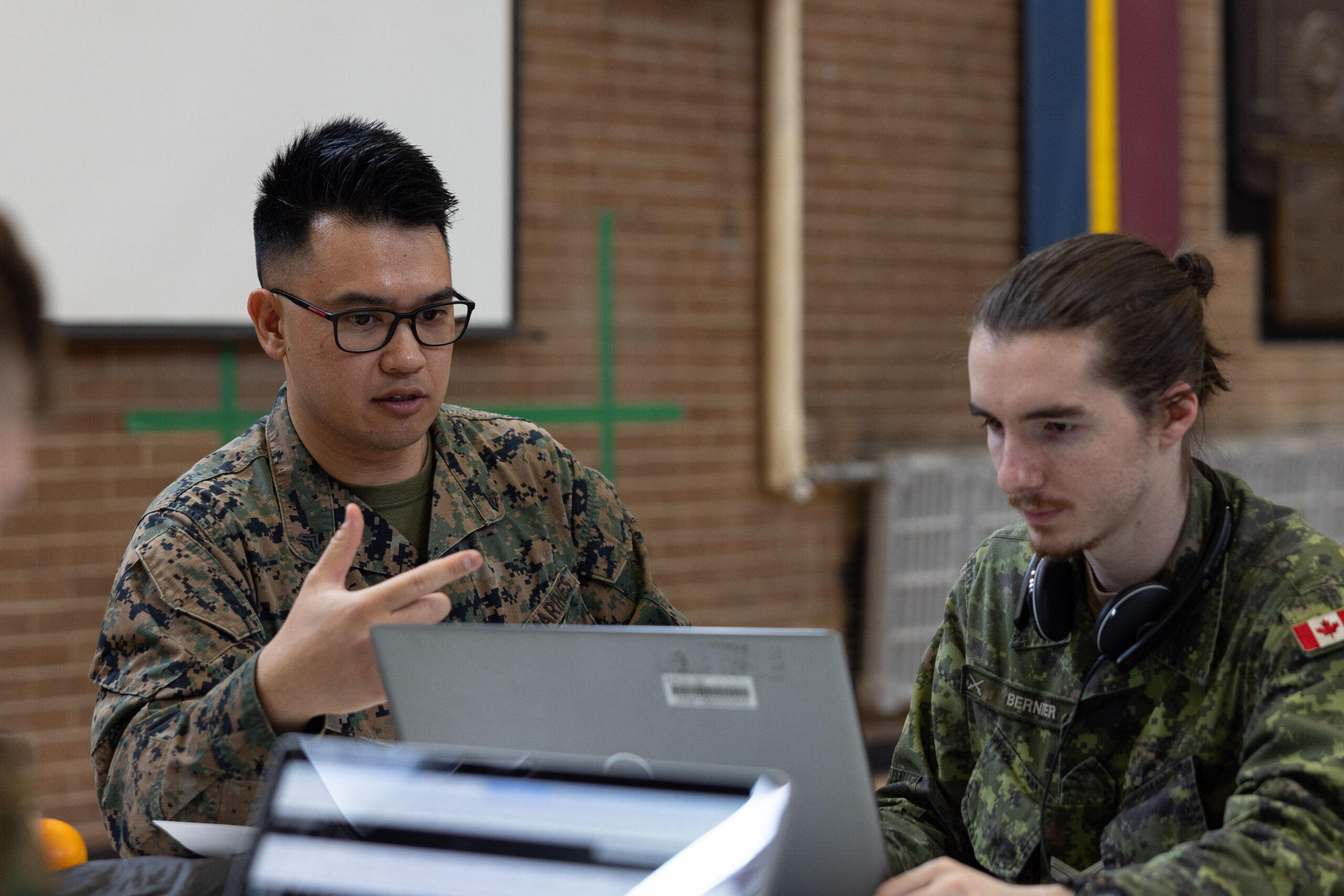 U.S. Marine Corps Cpl. Miles Young (left), data systems administrator, Defensive Cyberspace Operations, Company A, 6th Communication Battalion, Marine Forces Reserve, discusses his network hacking plan with a Canadian Army service member during Cyber Harmony 24 at The Royal Montreal Regiment, Quebec, Canada, April 28, 2024. This exercise allowed Reserve Marines to integrate with their active duty counterparts and joint partners to help develop practices in defense against cyber attacks.
