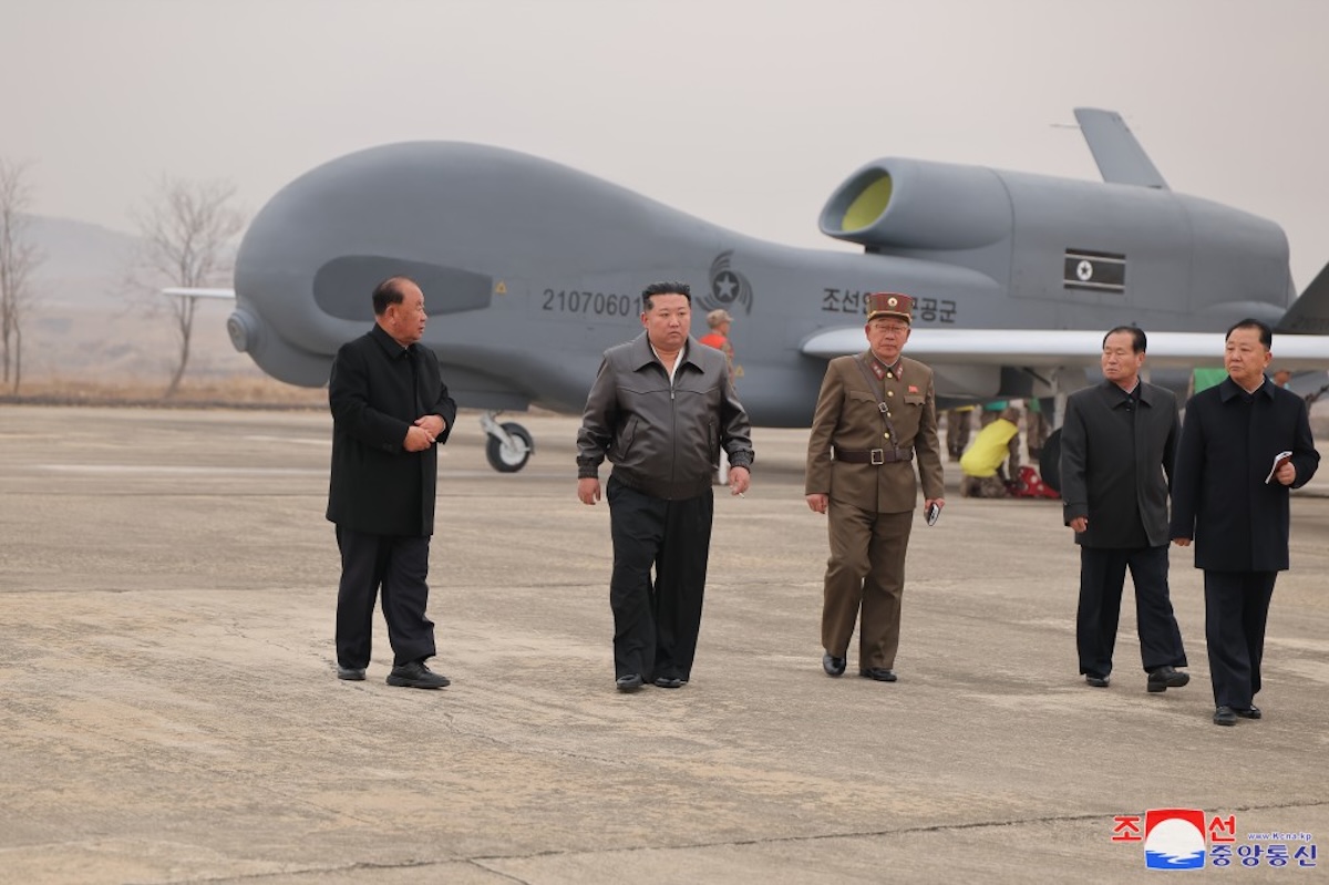 North Korean leader Kim Jong Un walking with cohorts with a suicide drone in the background