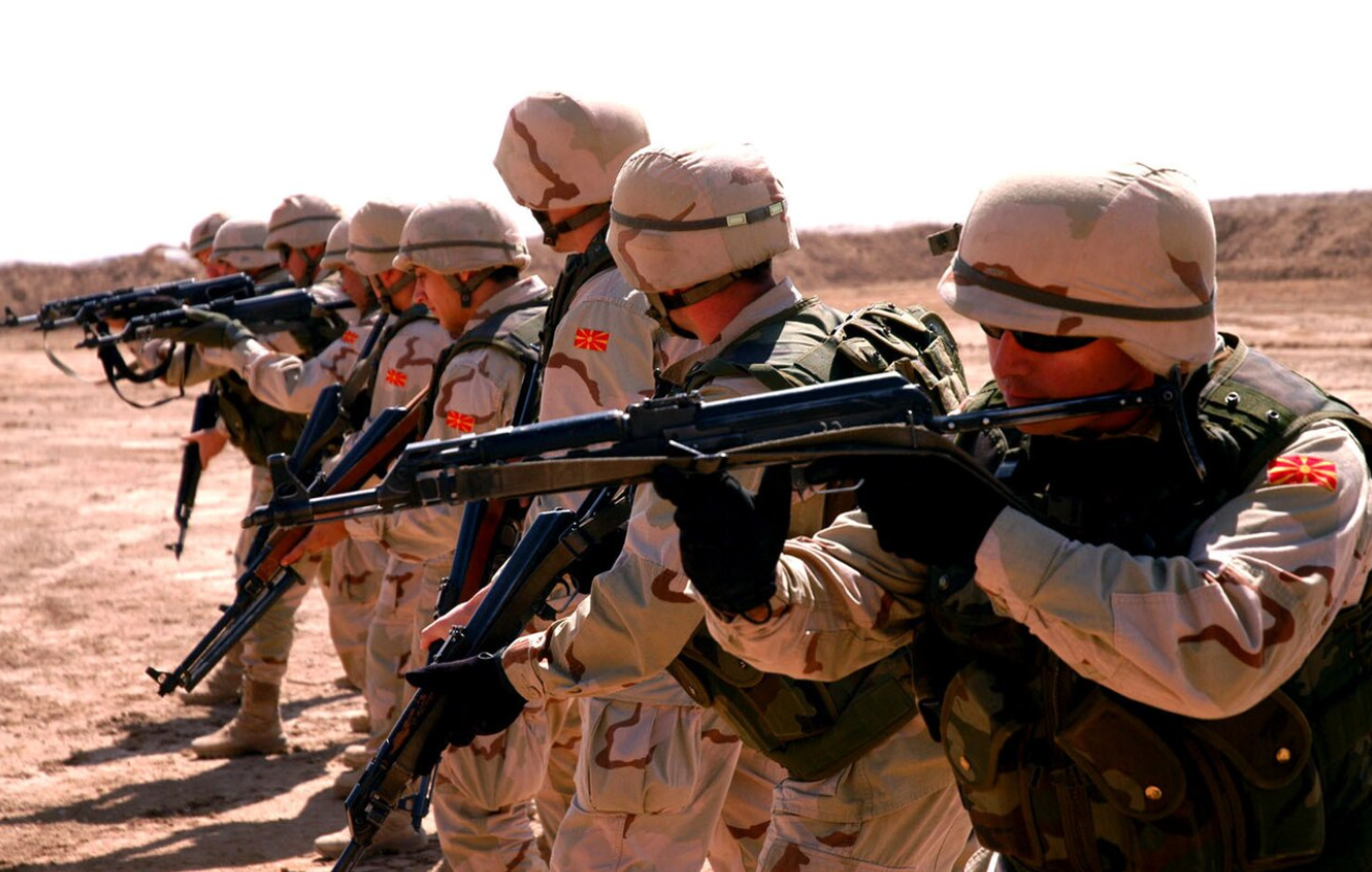 Seven soldiers from the Army of North Macedonia are seen pointing their rifles at something out of frame to the left. They are all wearing brown camo fatigues.