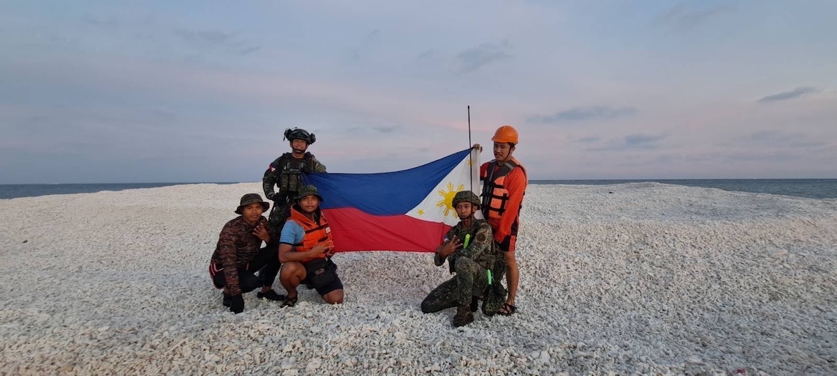 The Philippine Coast Guard holding the country's flag over the disputed Sandy Cay reef in the South China Sea.