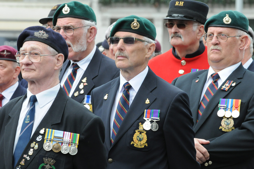 A group of British Armed Forces veterans are seen grouped together on a parade. They are all wearing suits and medals, as well as berets.