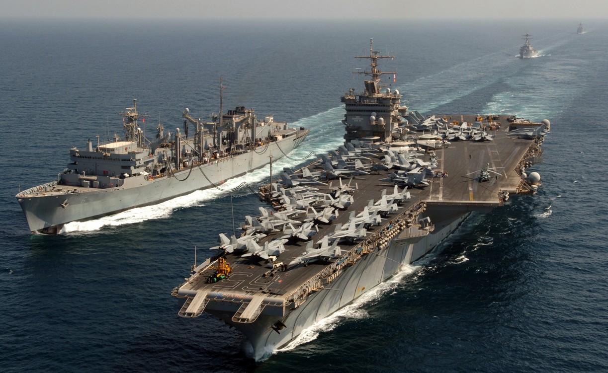 The warship USS Enterprise is seen sailing across deep blue waters. The aircraft carrier has dozens of fighter planes and a helicopter taxied on it.