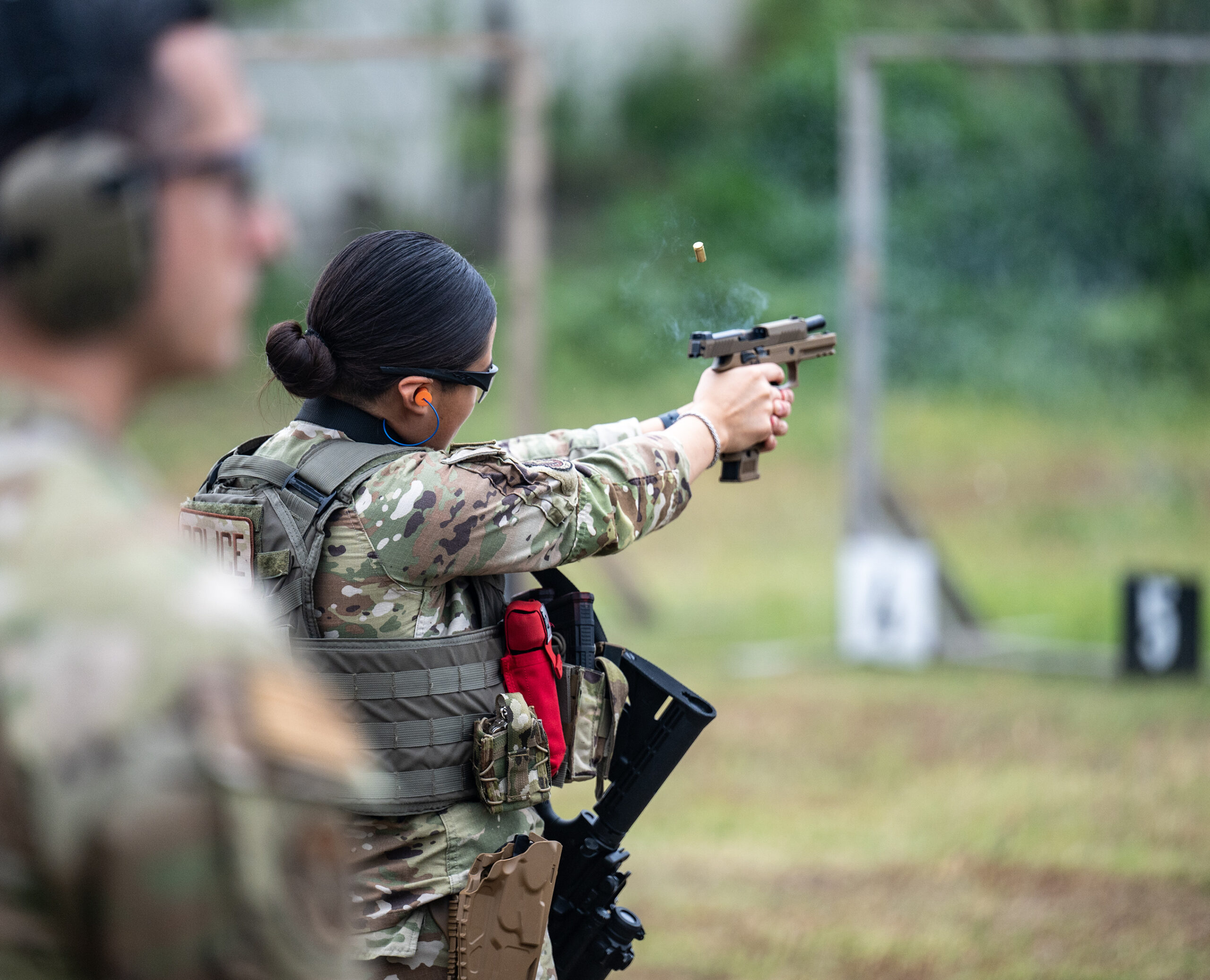 Airman Mia Marquez, 802nd Security Forces Ssquadron installation access controller, fires an M18 handgun at paper targets while U.S. Air Force Tech. Sgt. Justin Hains, 802nd Security Forces Squadron noncommissioned-officer-in-charge of training, observes the firing range while during sustainment firing training at Joint Base San Antonio-Lackland, Texas, April 9, 2024. Students participate in this training to better understand the weapons systems while also completing drills that require different firing positions to maintain proficiency and develop their firearms skills. (U.S. Air Force photo by Brian Boisvert)