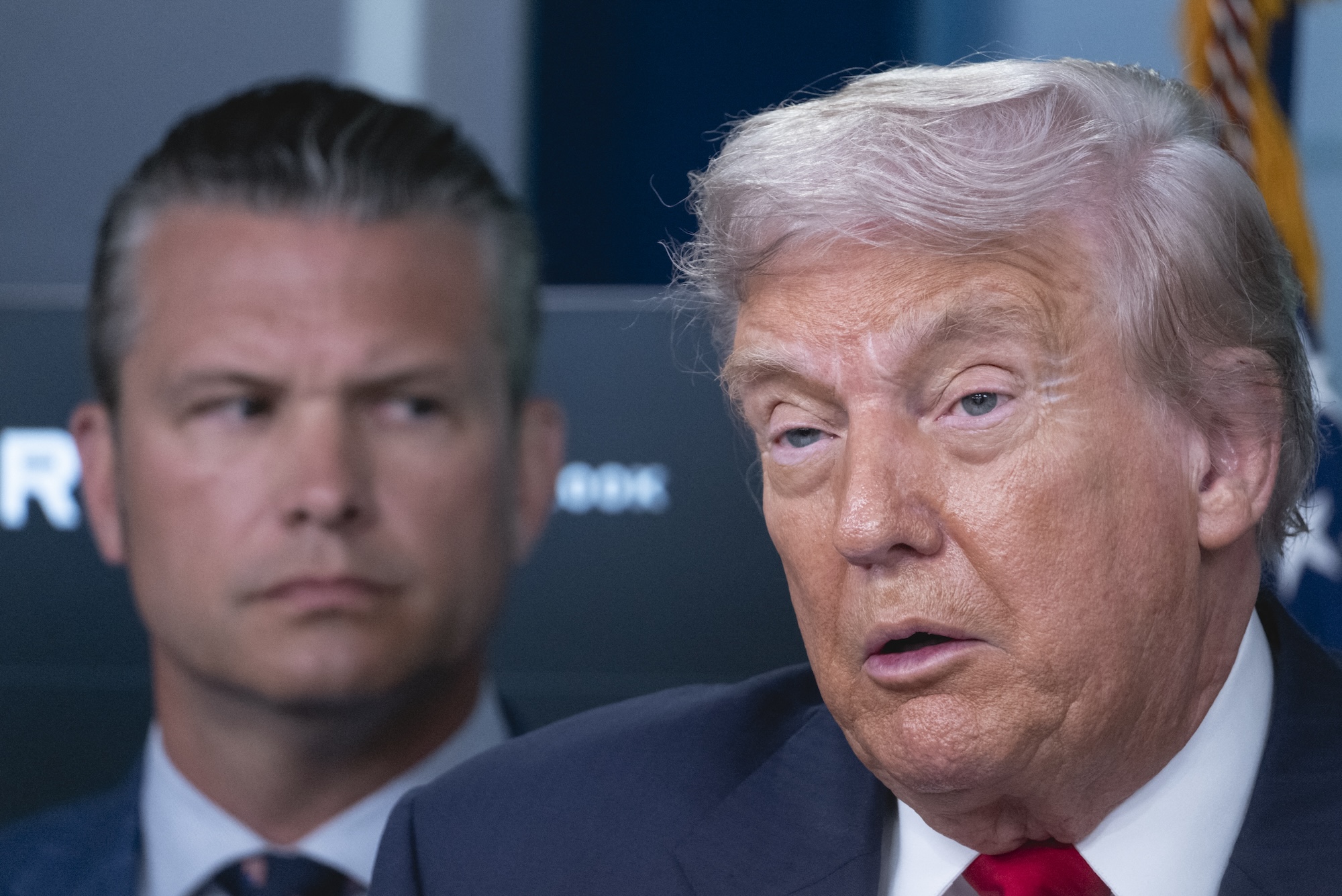 President Donald Trump speaks to reporters as Defense Secretary Pete Hegseth stands behind him