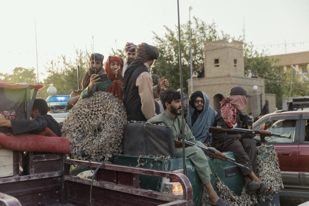 Taliban personnel holding guns and phones while riding on the back of a truck