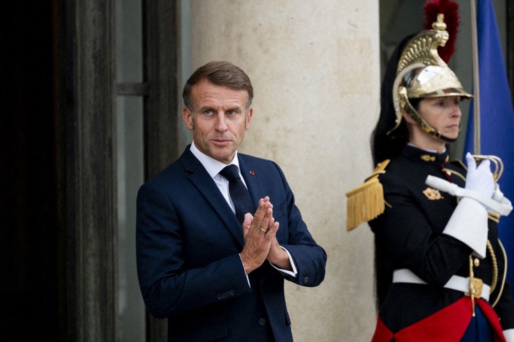 French President Emmanuel Macron rubbing his hands with a royal guard in the backgorund