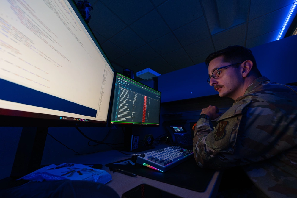 A soldier in a dark room looking at two monitors