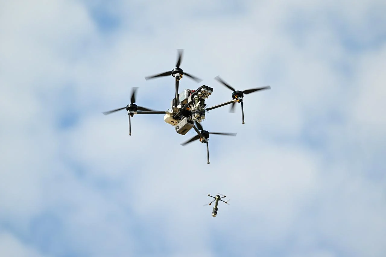 A brightly lit image of the D155 drone releasing a smaller drone while in the air with a cloudy background