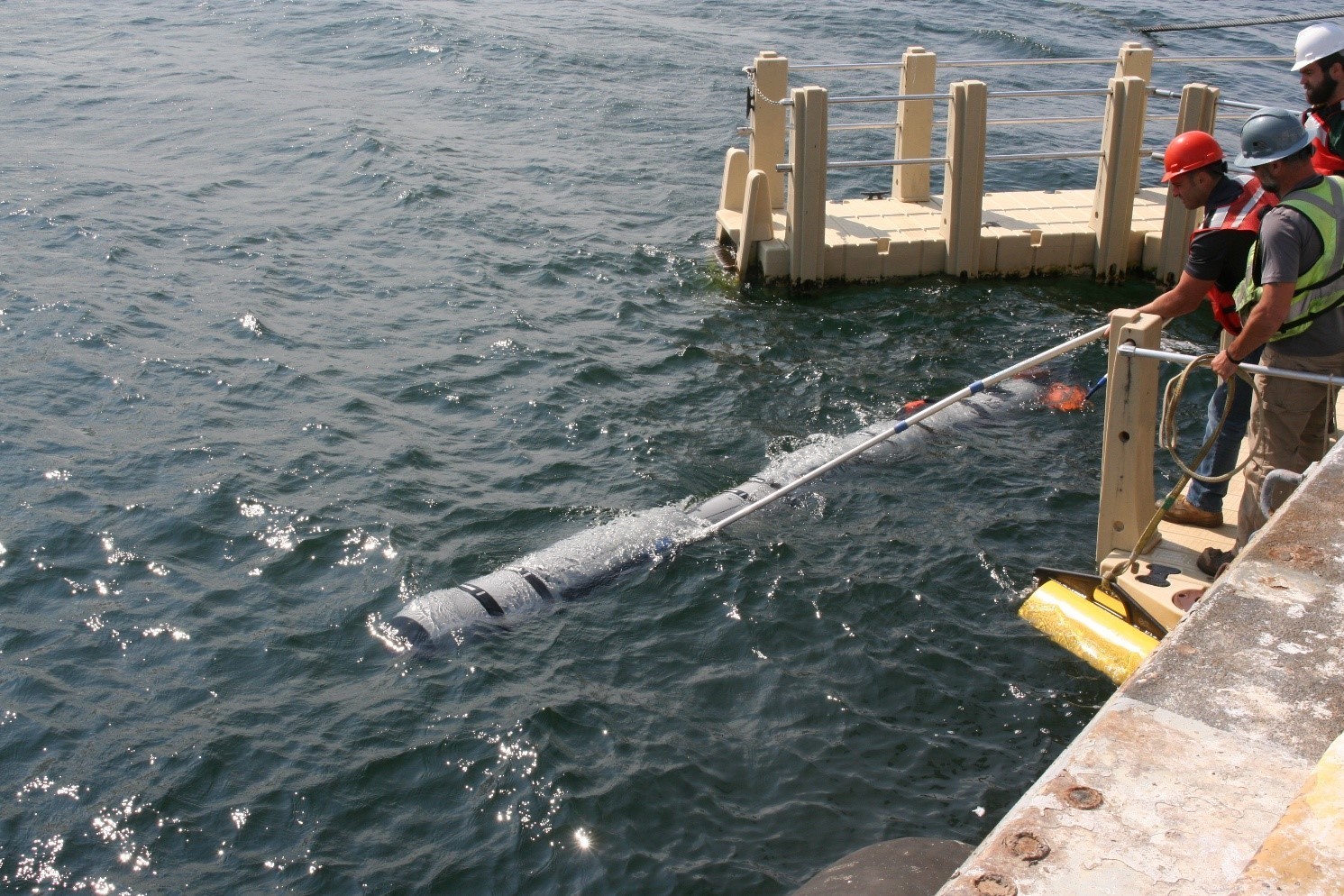 The REMUS 620 being prepared for launch with workers standing on a pier