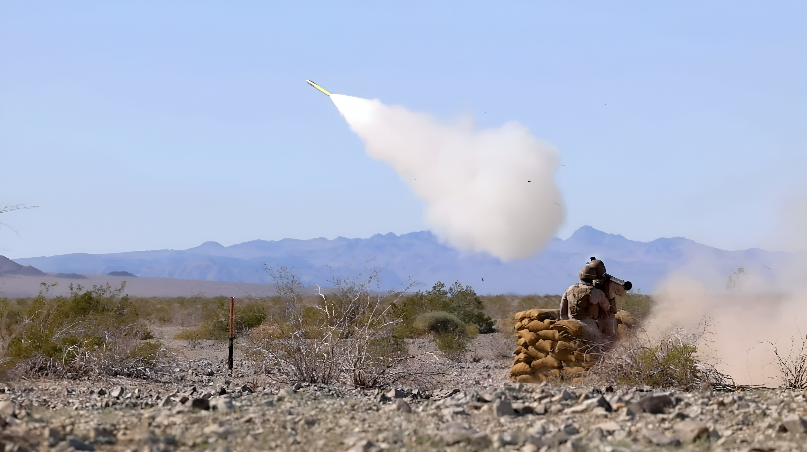 A soldier firing a missile in a sandy environtment with a clear daylight background