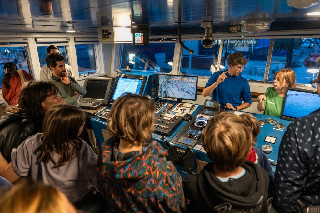 Greenpeace activists on a boat, gathered around a laptop, engaged in a discussion about environmental initiatives