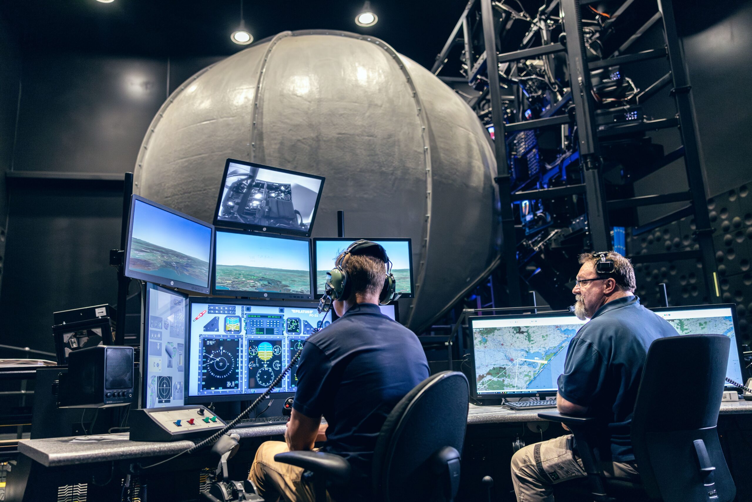 Two people in a control room operate flight simulators with multiple screens displaying maps and cockpit views, creating a focused and high-tech environment.