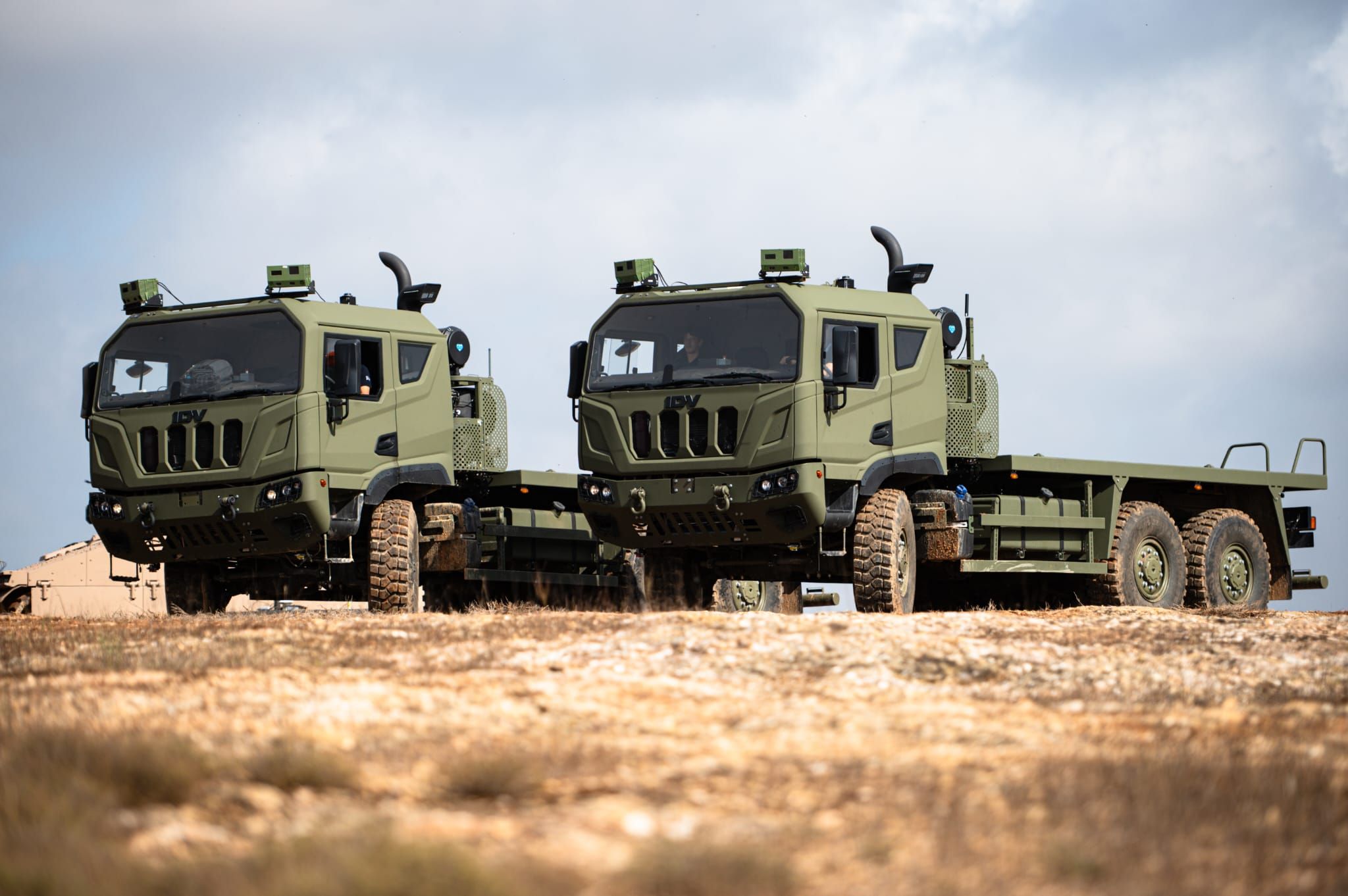 A brightly lit photo of two green trucks with the Naviground system with a light brown soil surface