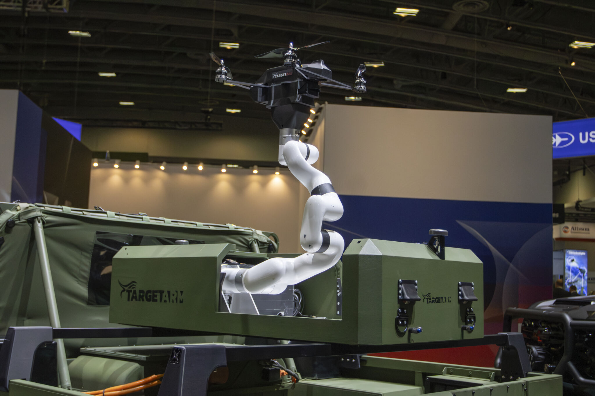 Robotic arm mounted on a military vehicle demonstrating its ability to launch and recover small drones in a defense technology exhibit