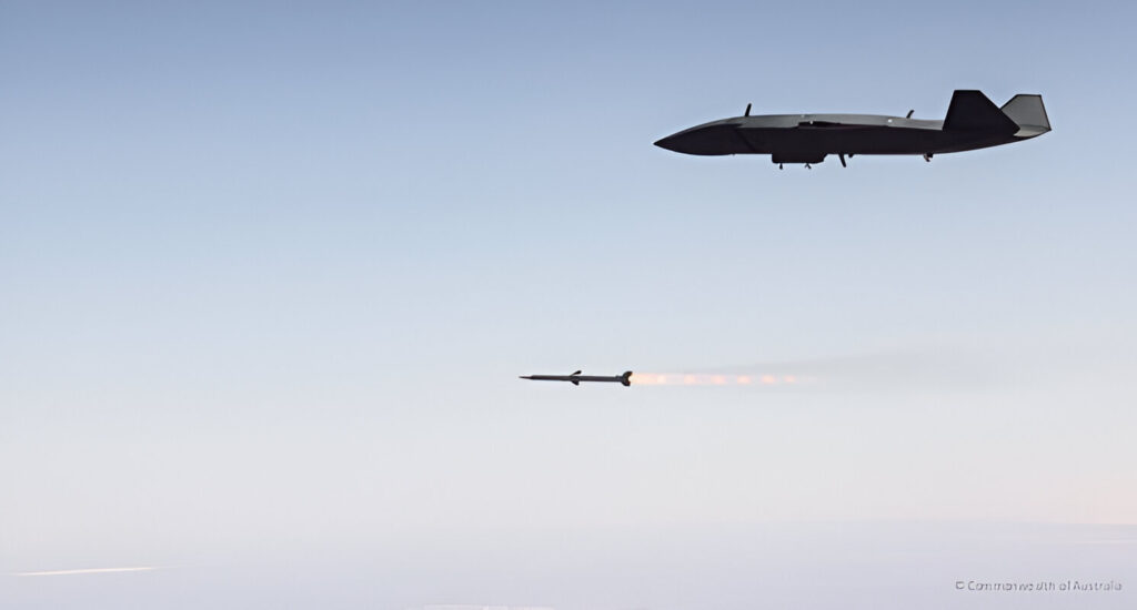 An MQ-28 Ghost Bat flies high above the ocean as it launches a missile, captured mid-flight with the weapon’s exhaust trail glowing against the clear sky