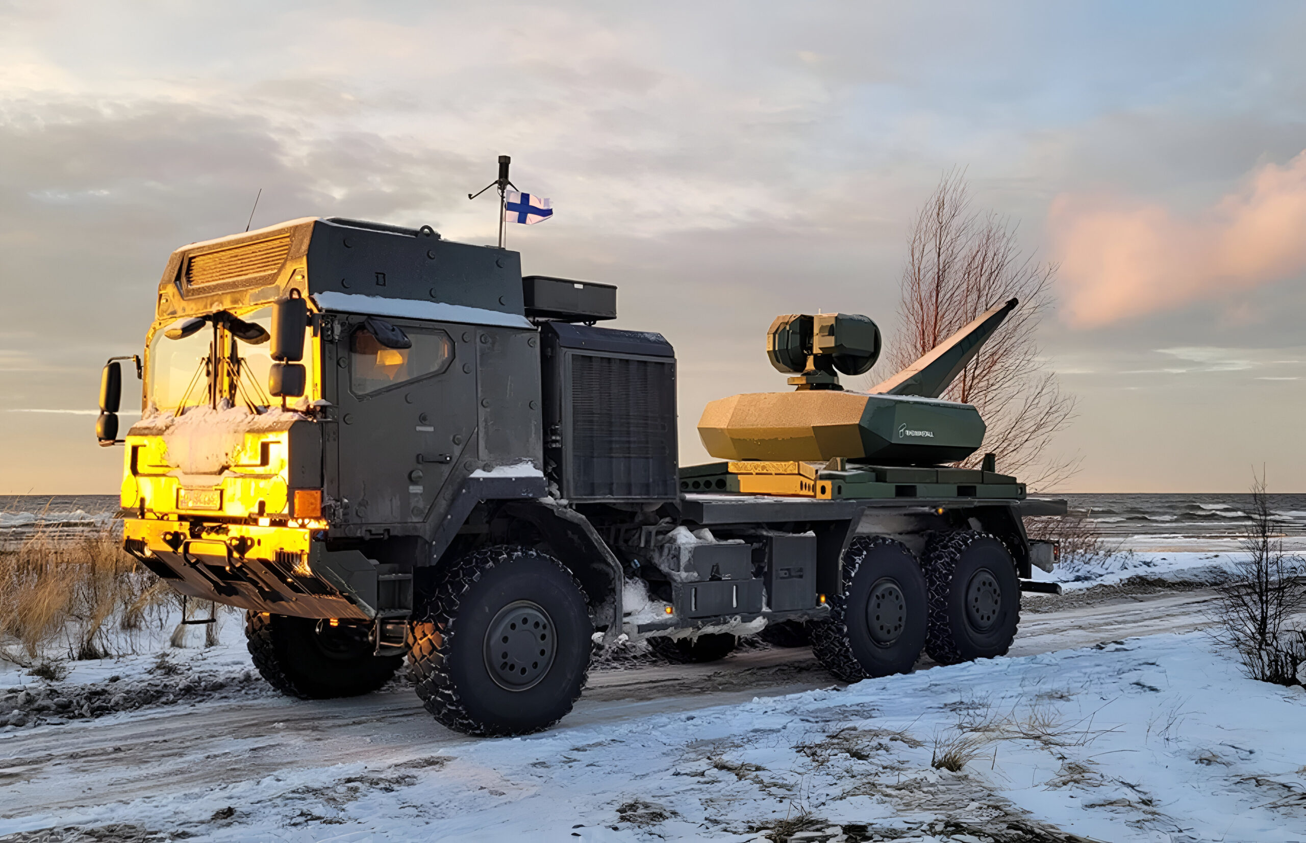 A Finnish Army military truck fitted with the Skyspotter counter-drone system, shown during a winter field test near a coastline, with the Skyspotter sensor mast and turret mounted on the rear platform under low evening light