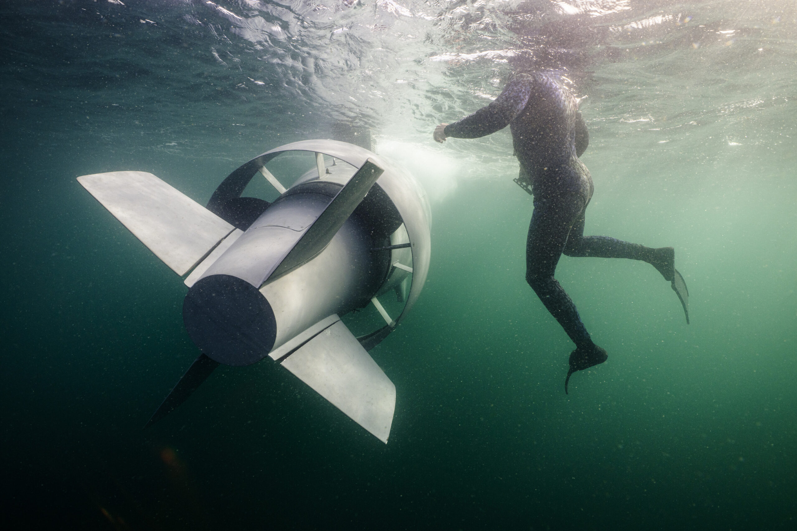 GreyShark AUV cruising underwater beside a diver, showing the autonomous vehicle’s streamlined design, rear fins, and propulsion system during subsea operations
