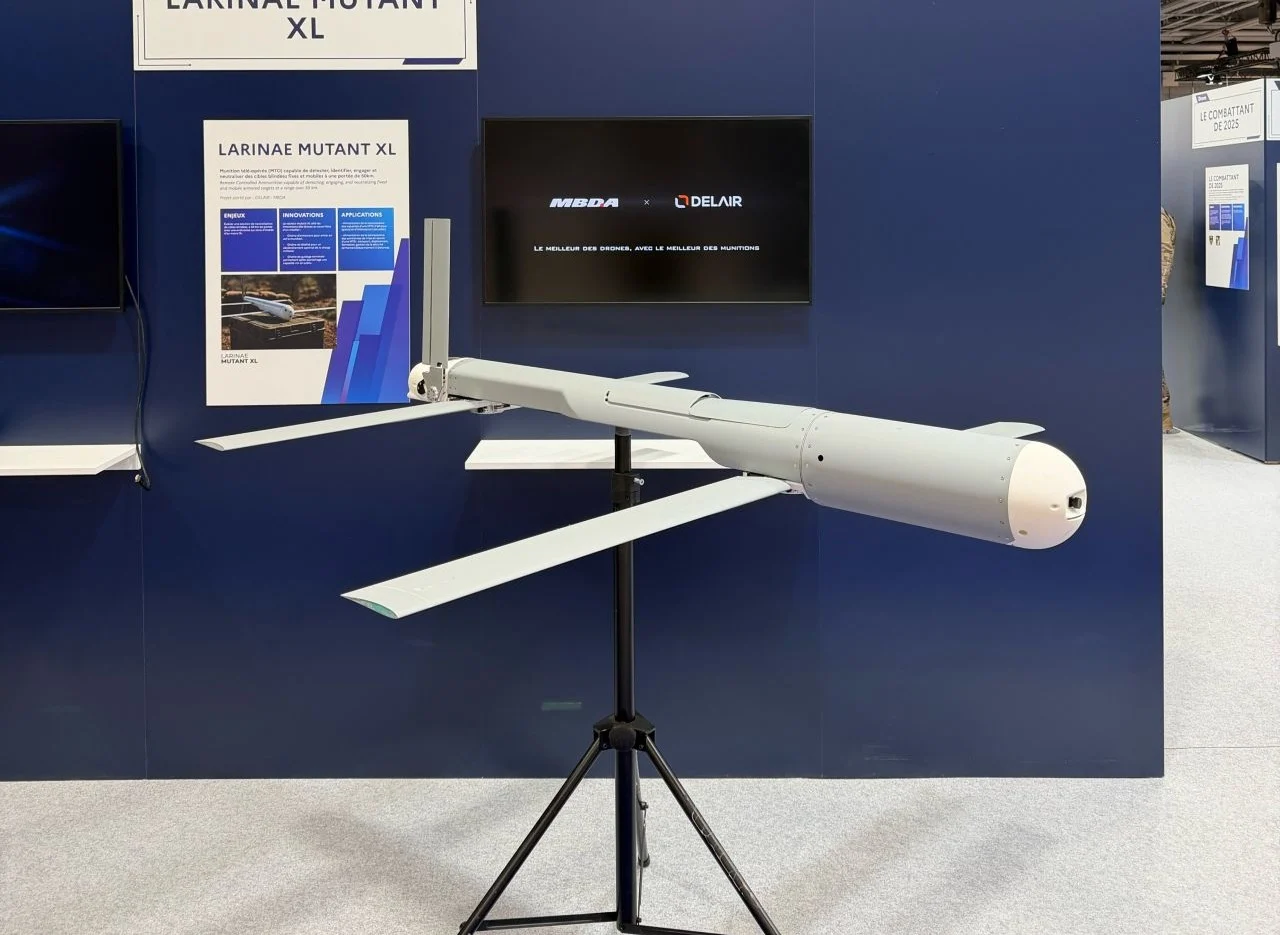 Mutant XL loitering munition displayed on a stand at an exhibition, showing its long airframe, extended folding wings, and streamlined nose against a blue MBDA–Delair booth backdrop