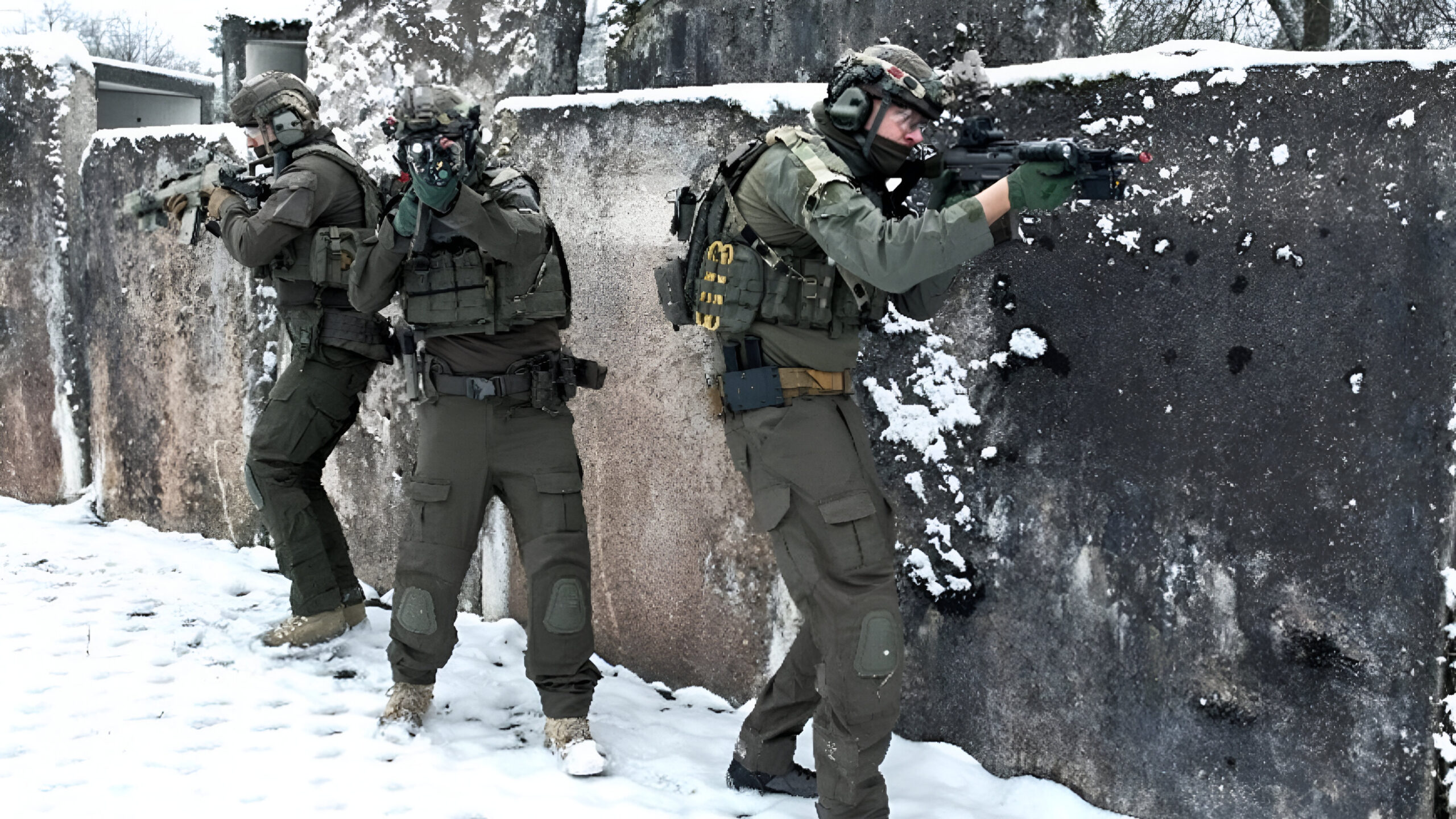 Soldiers in winter gear conduct live training behind a snow-covered concrete barrier, aiming their rifles while advancing in a coordinated formation