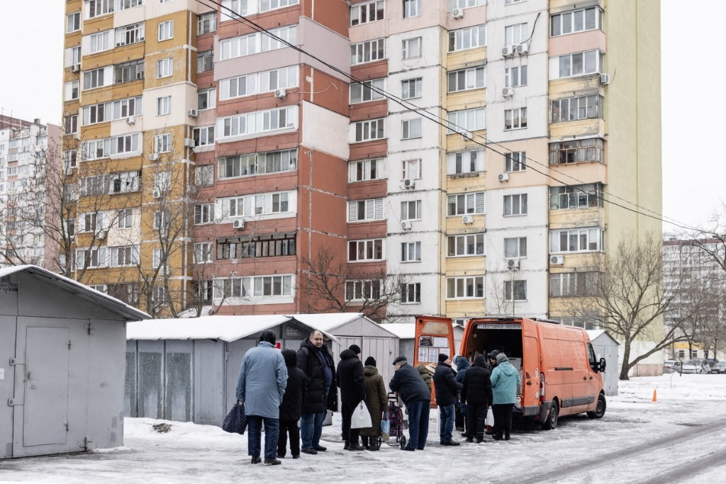 People wait in line for a mobile delivery of essential goods in the Troieshchyna district of Kyiv, Ukraine on January 30, 2026.