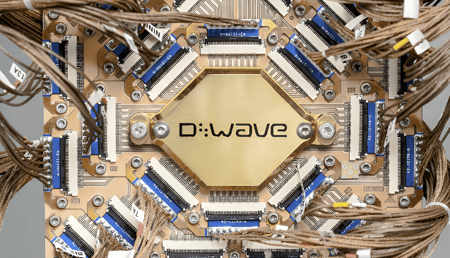 Close-up of a D-Wave quantum processor chip mounted on a copper-colored circuit assembly, with dense wiring and connectors surrounding the central quantum module.