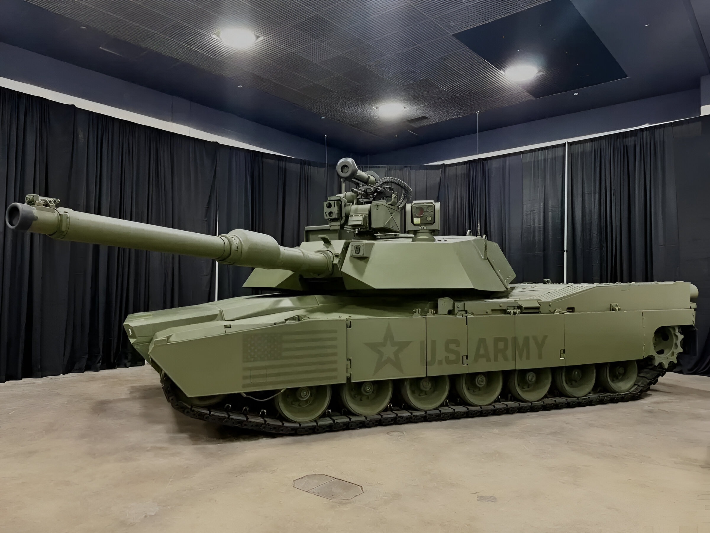 M1E3 Abrams main battle tank displayed indoors, showing its upgraded turret, long main gun, reinforced armor, and U.S. Army markings under exhibition lighting.