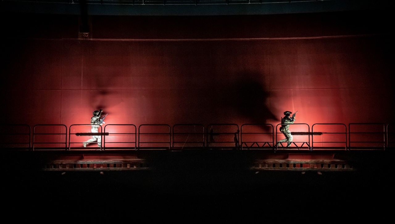 NATO special operations forces conduct a nighttime training exercise during Exercise Nighthawk 21, moving along an industrial platform under red lighting.