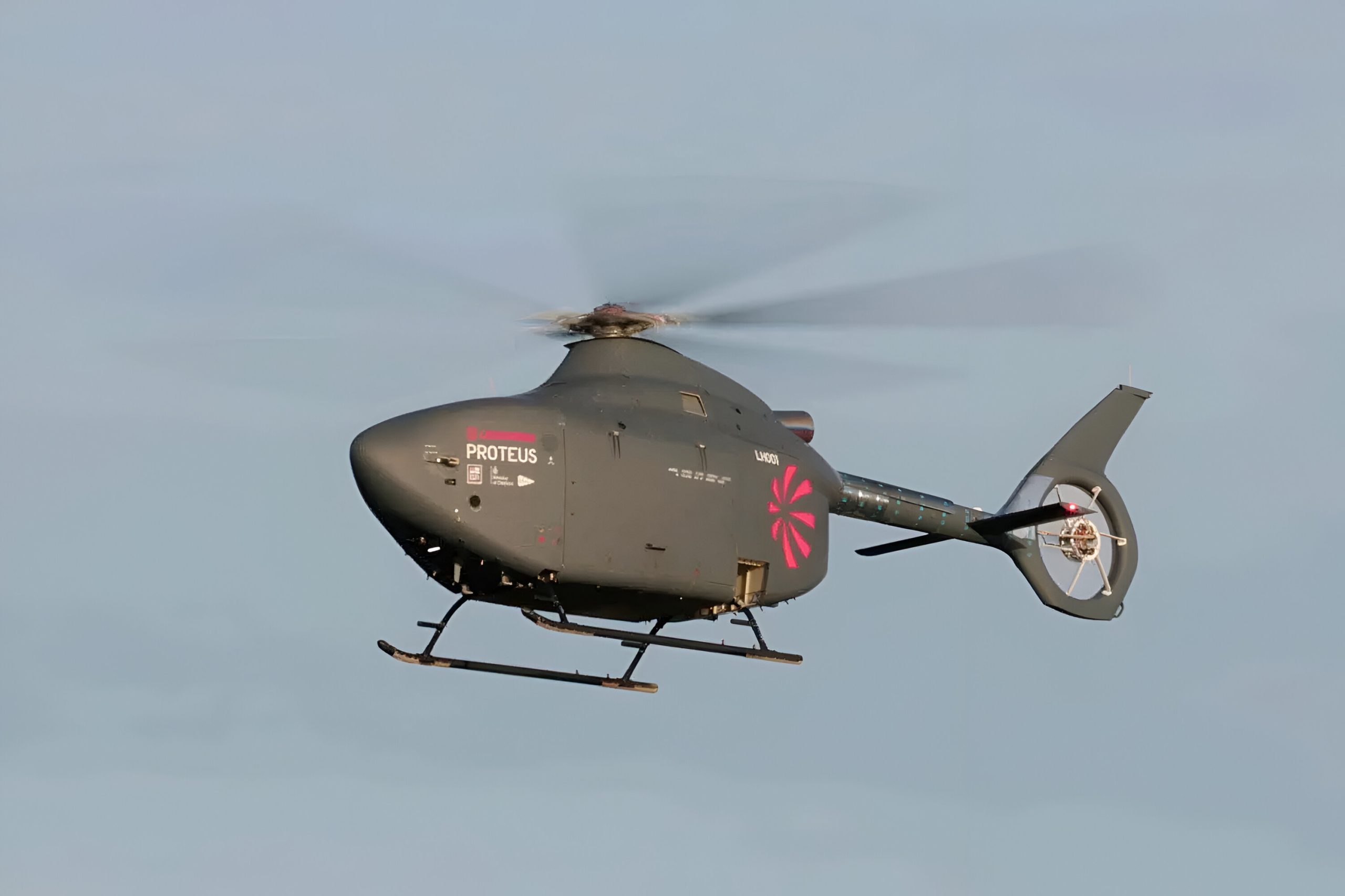 A small autonomous helicopter flying through the air against a clear blue sky.